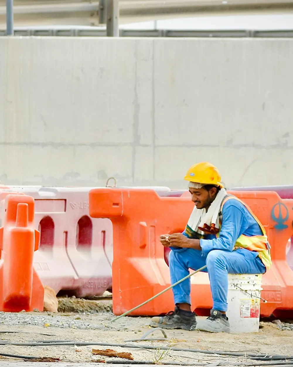 Trabalhador de obra com capacete, sentado junto às barreiras, a usar o telemóvel